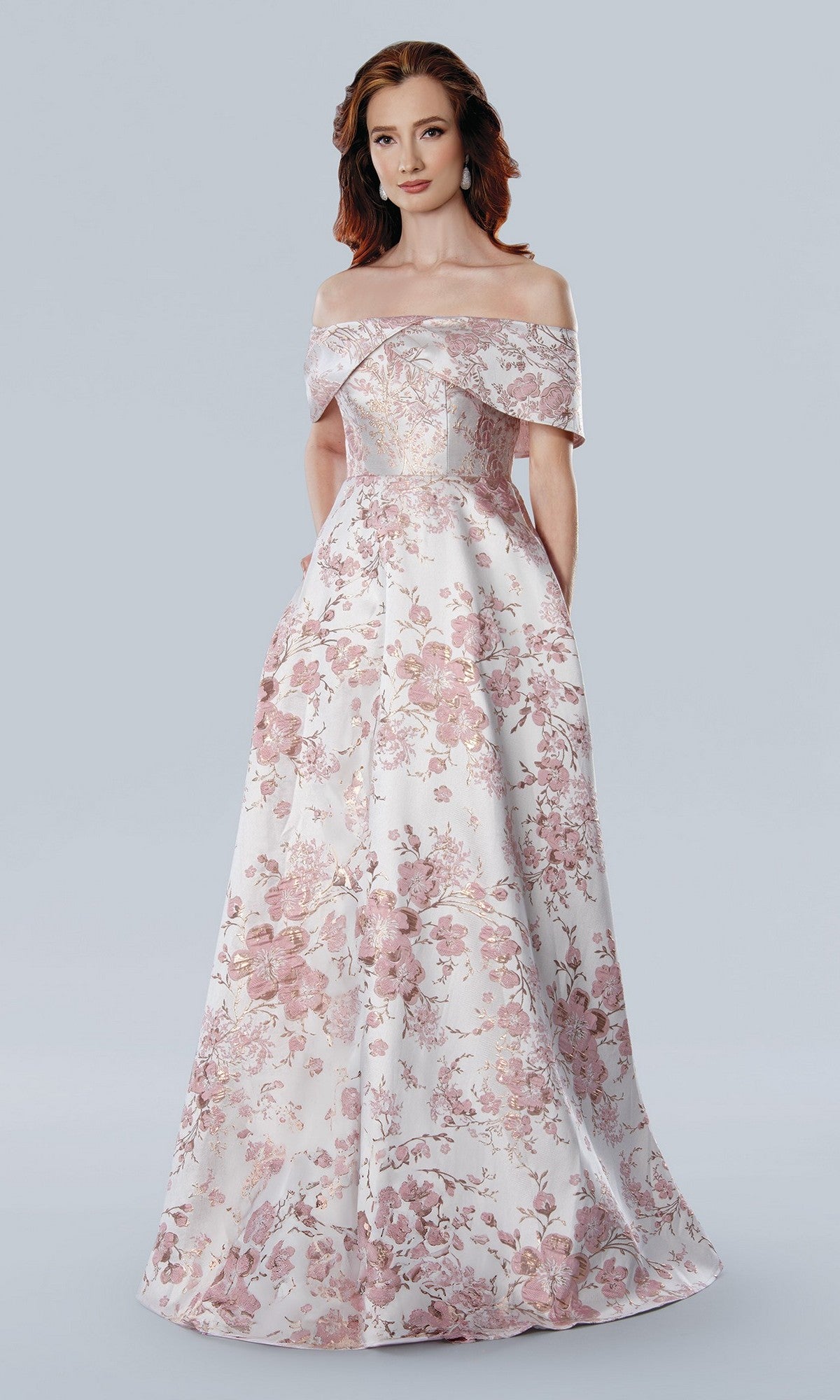 A woman stands against a plain light gray background wearing the Stella Couture 25303 long formal dress in rose, featuring an off-the-shoulder neckline and floor-length floral jacquard fabric.